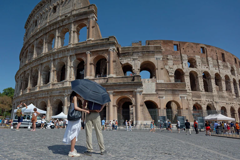 A couple shield themselves from the sun under an umbrella outside the Colosseum in Rome