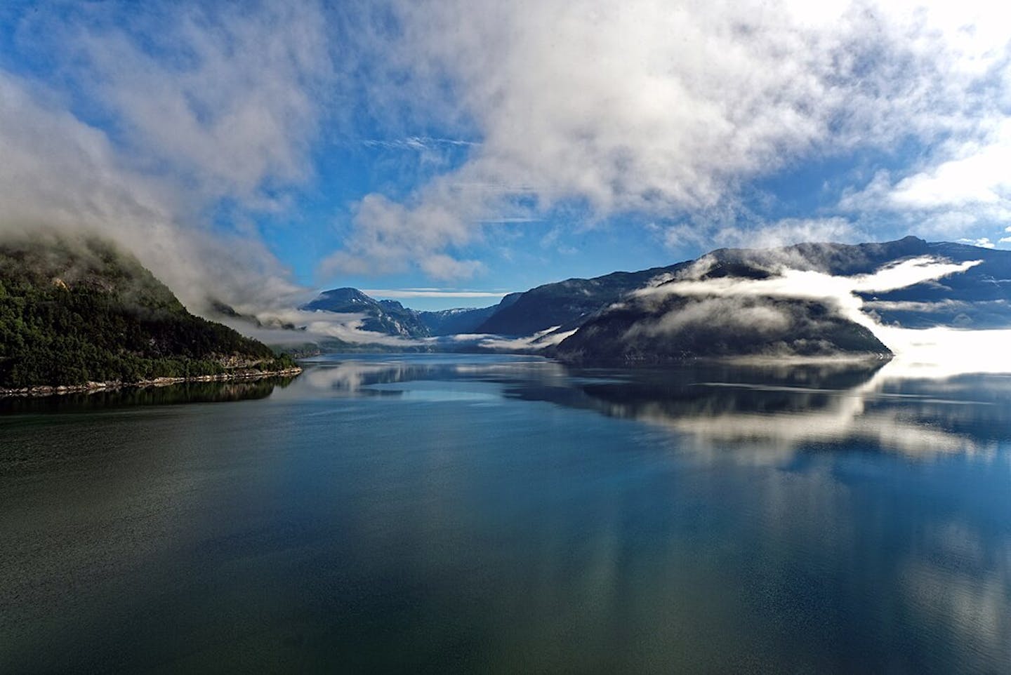 Imagen de un fiordo con nubes que se meten casi en el agua.