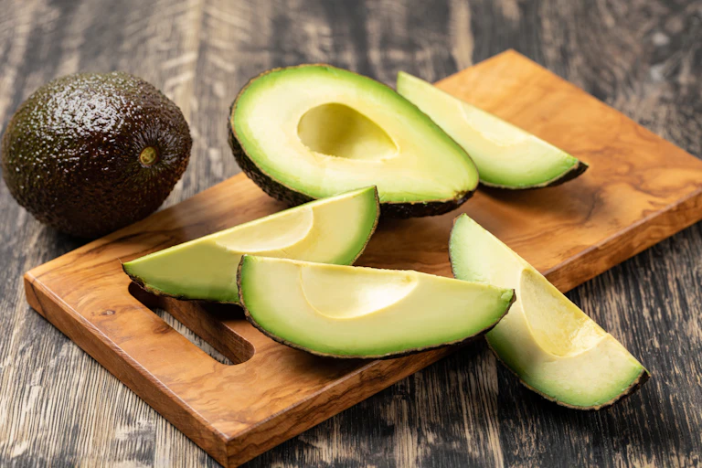 A dark green whole fruit and some pale green sliced open fruit on a wooden board