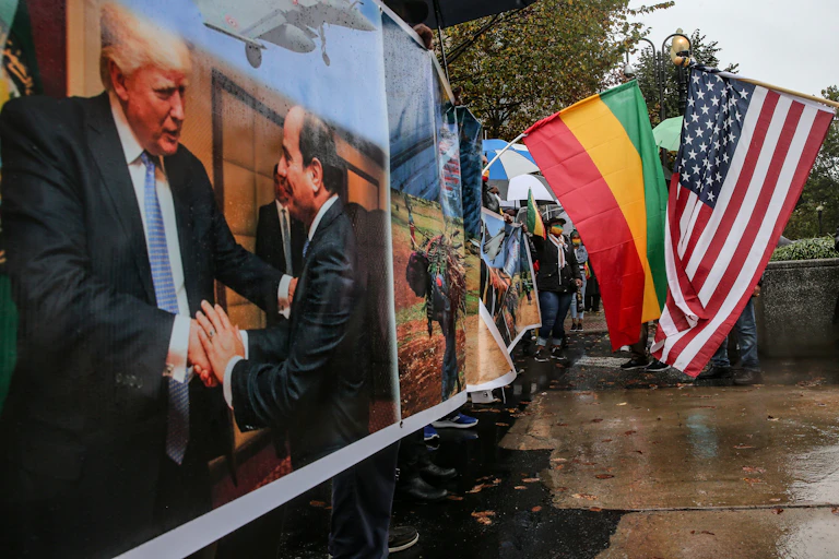Two large flags are flown next to a poster of two men shaking hands.