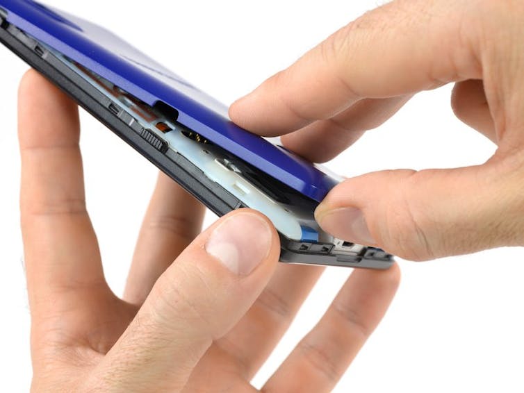 A person’s fingers touch the back and front of a smartphone as that person opens its back cover