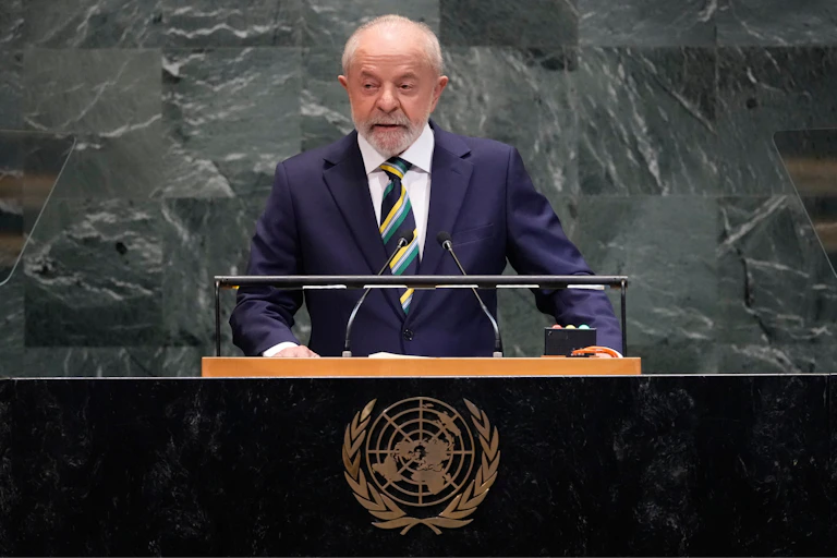 An 80-year-old white man in a suit speaking at a podium in the United Nations plenary hall.