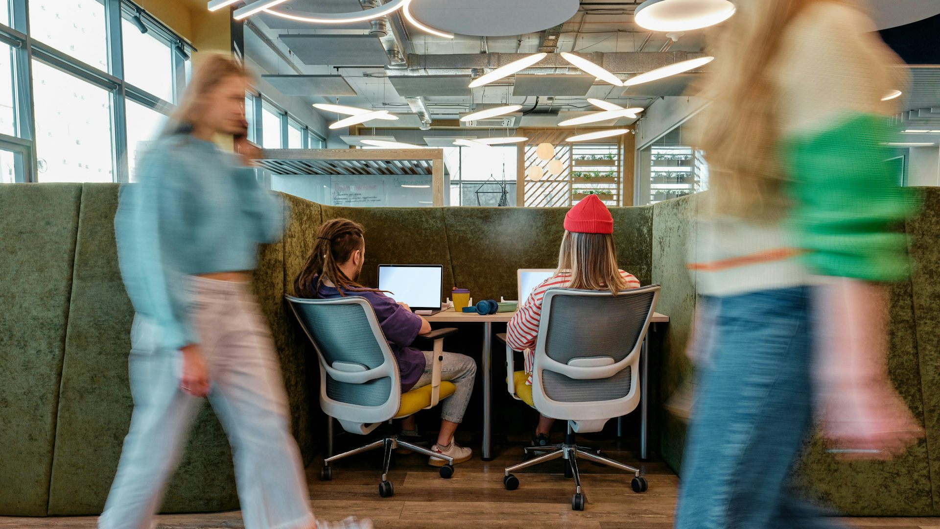 Deux jeunes adultes vus de dos, travaillant sur des ordinateurs portables à un bureau.