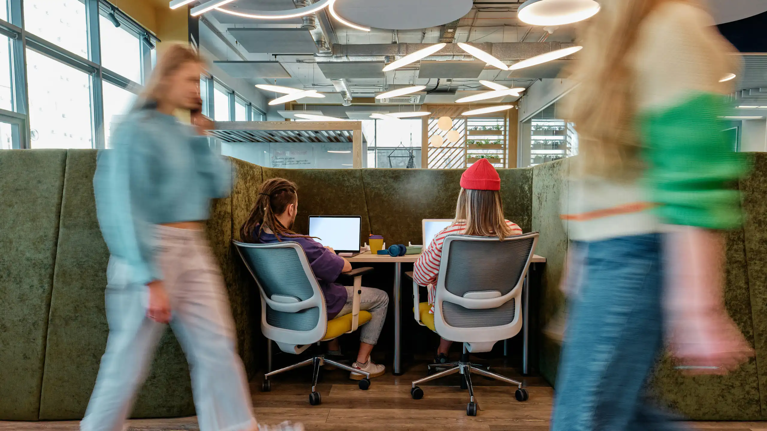 Deux jeunes adultes vus de dos, travaillant sur des ordinateurs portables à un bureau.