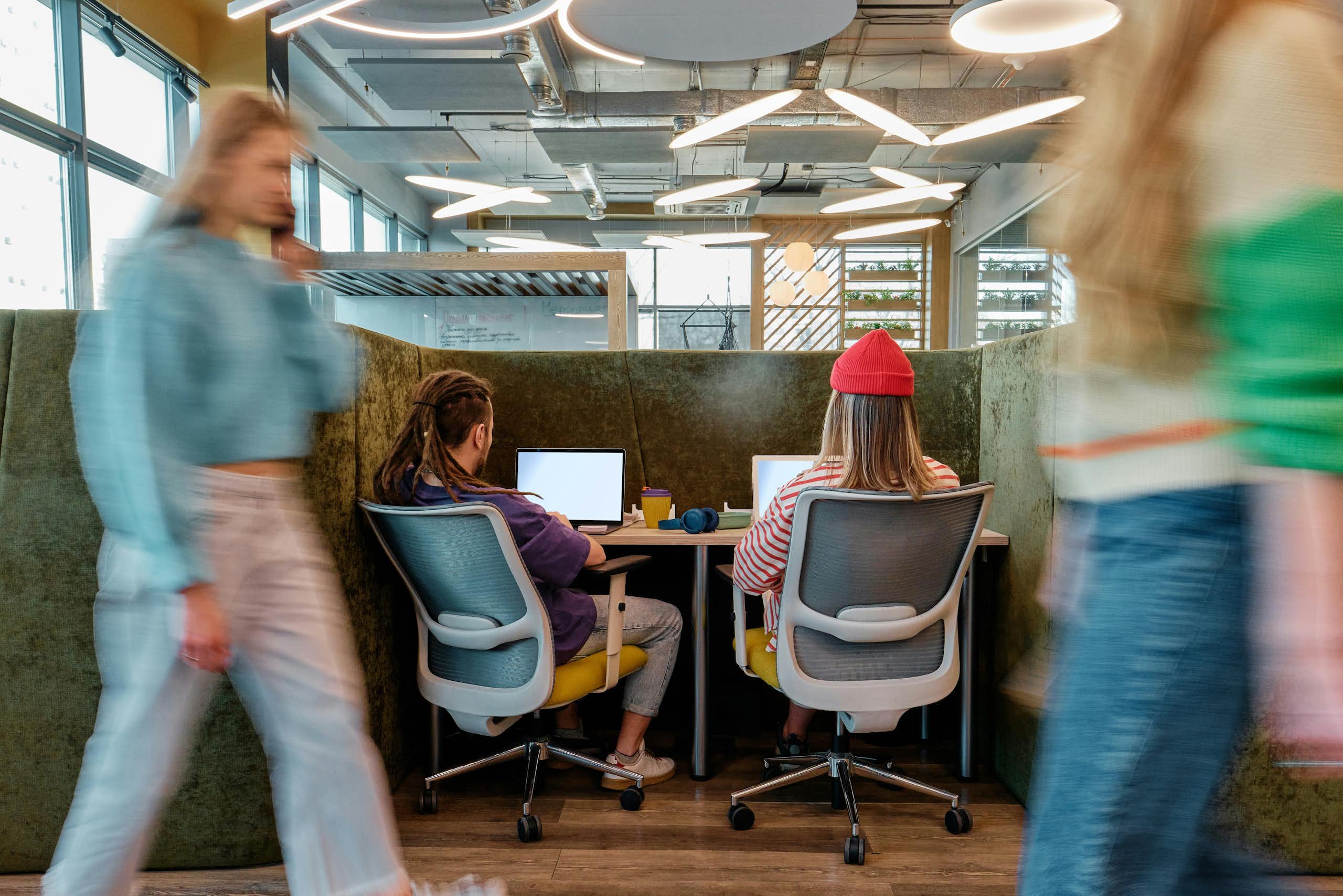 Deux jeunes adultes vus de dos, travaillant sur des ordinateurs portables à un bureau.