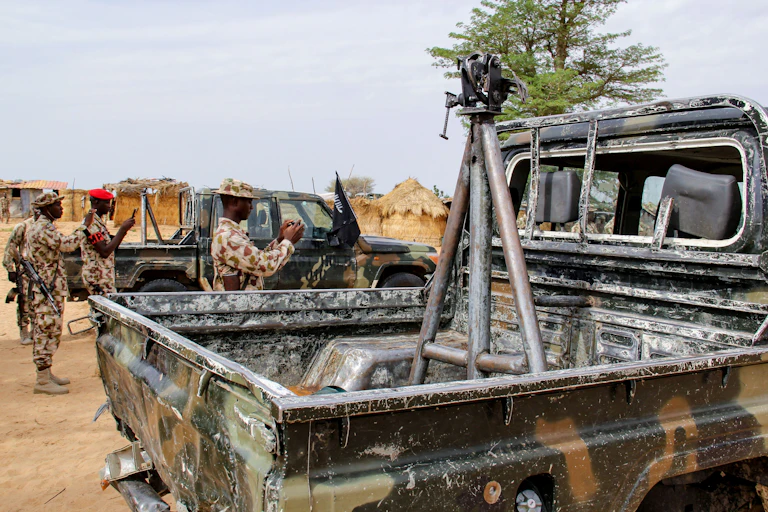 Soldiers in camouflage uniform standing around a burnt vehicle