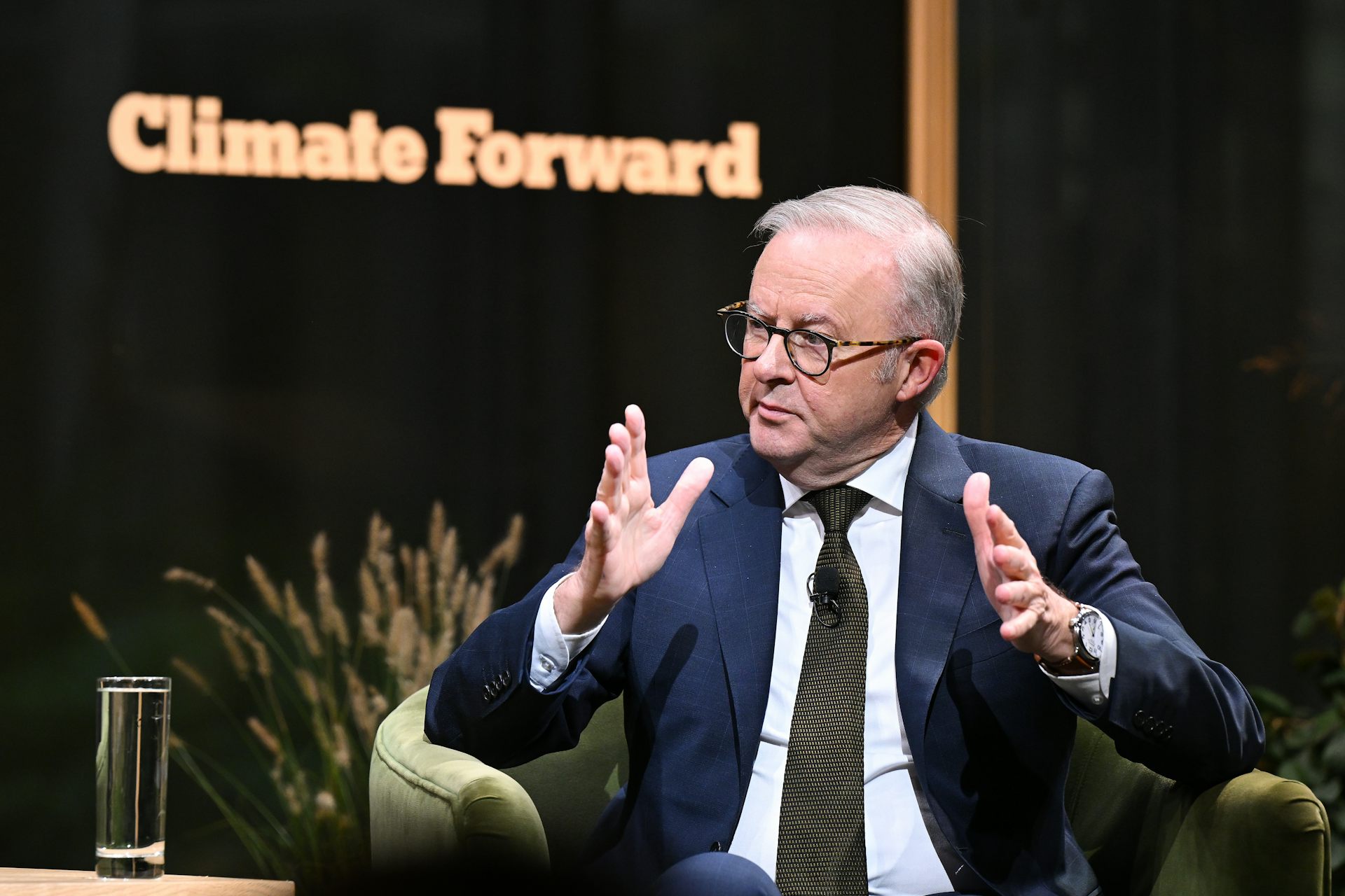 A man in a suit gestures in front of a sign reading 'Climate Forward'