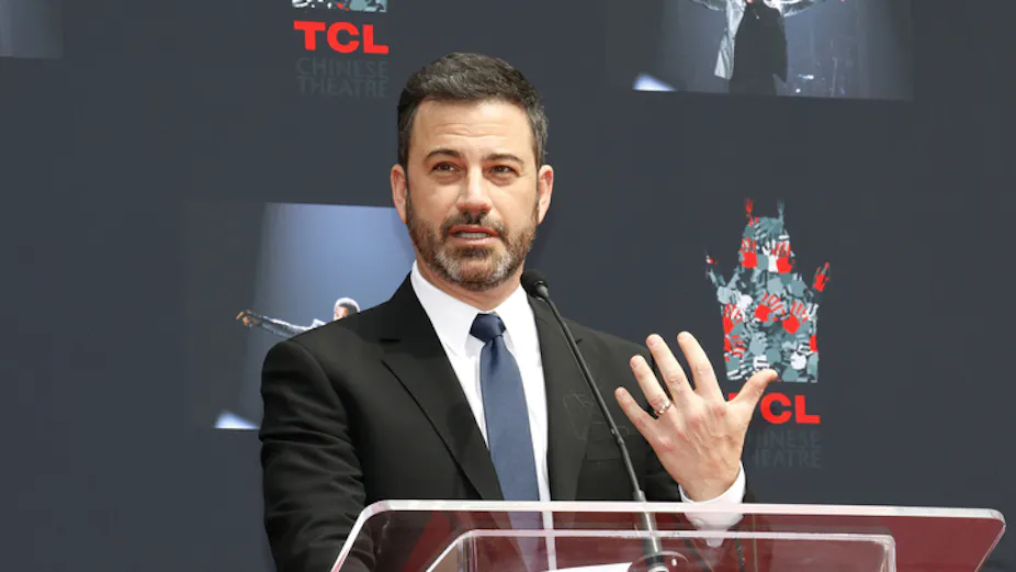 US comedian Jimmy Kimmel gestures with his hand while standing at a podium.
