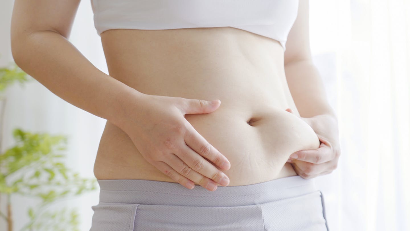 A woman pinching her belly, showing a roll of subcutaneous fat.
