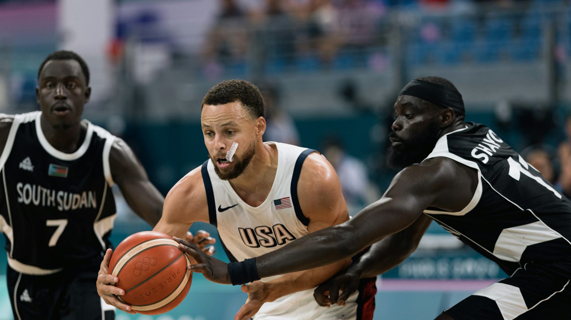 Two South Sudanese basketball players compete with American Steph Curry during a basketball game.
