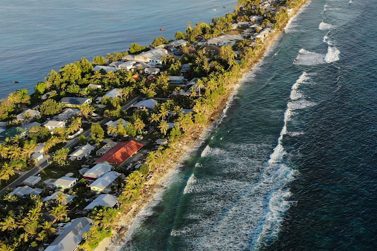 Uma ilha com casas nas margens da água, palmeiras e ondas em um lado.