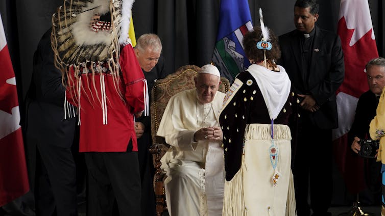 ¿Qué más necesitas después de disculparte las escuelas de vivienda del Papa? Acción apoyada, humildad y corazón 1 El hombre con vestidos blancos y la calavera blanca está sentada rodeada de mujeres con espacio blanco y plumas blancas y un hombre y un hombre con una pluma en la cabeza.