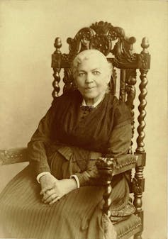 Elderly mulatto woman sitting in a large wooden chair with exquisite carvings.