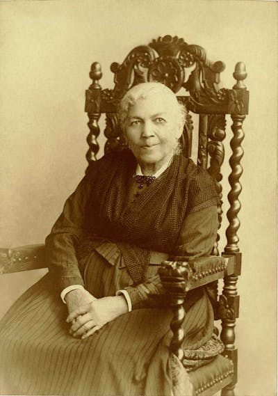 Elderly mulatto woman sitting in a large wooden chair with exquisite carvings.
