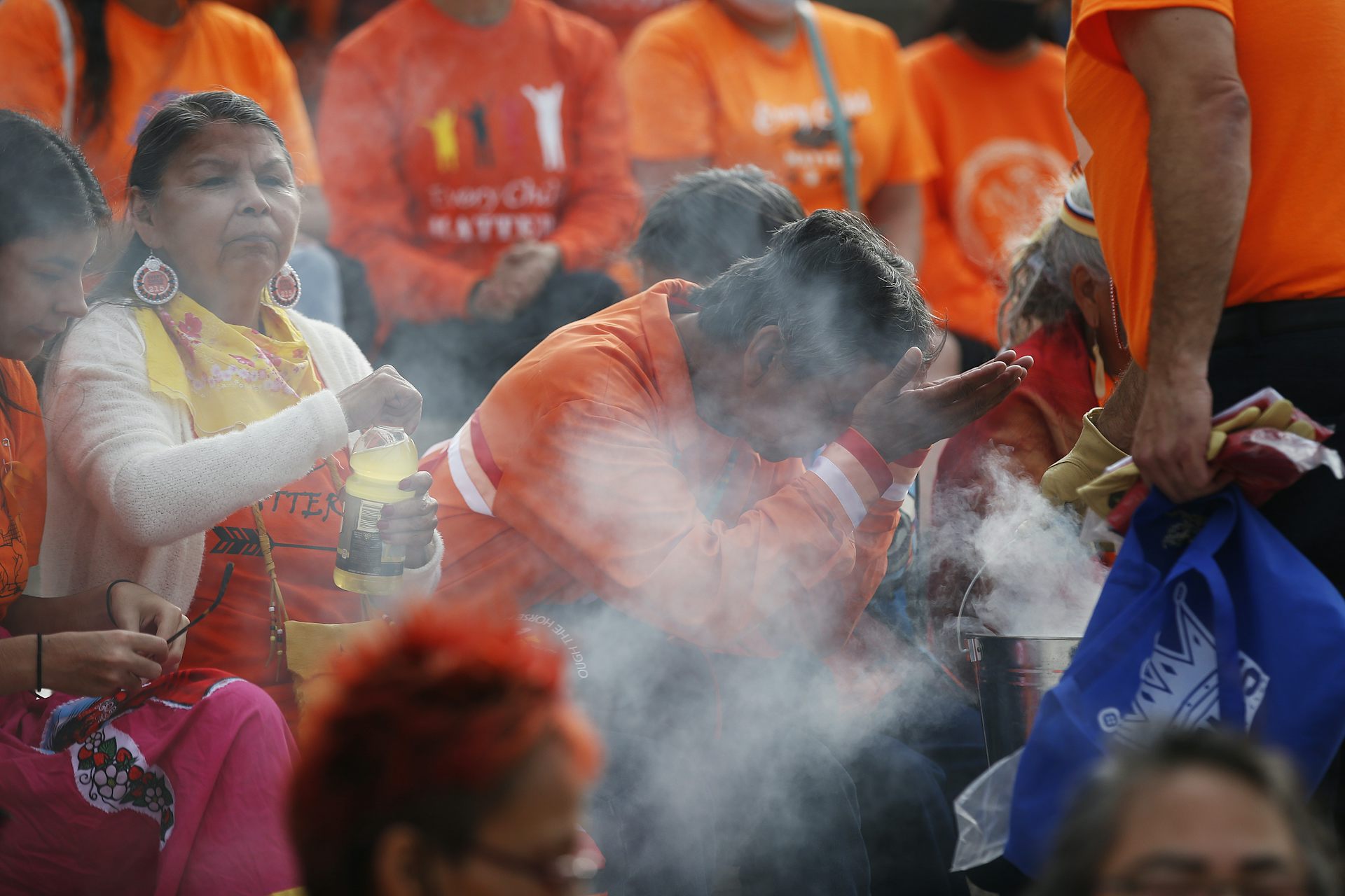 La persona se inclina en el humo de la cabeza arqueada, llevando la camisa naranja, en una multitud con otros con camisas naranjas.