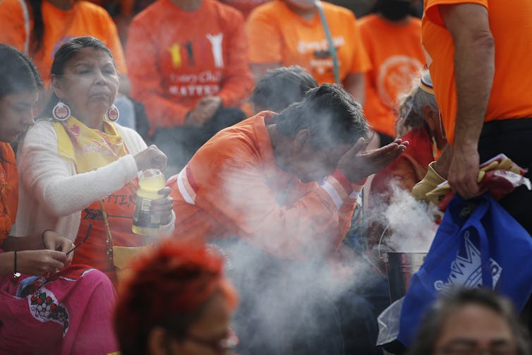 La persona se inclina en el humo de la cabeza arqueada, llevando la camisa naranja, en una multitud con otros con camisas naranjas.