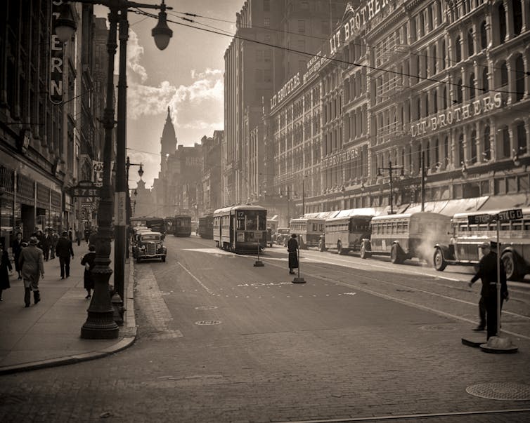 Sepia-toned photo of busy street in a commercial area of a city circa 1930s