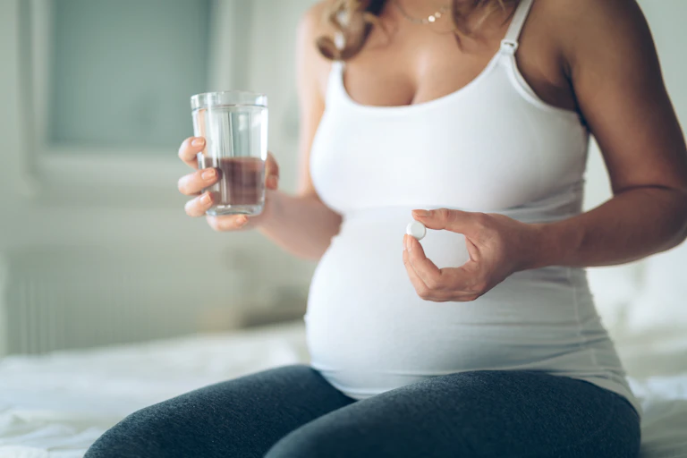 Photo d’une femme enceinte qui tient une pilule et un verre d’eau.