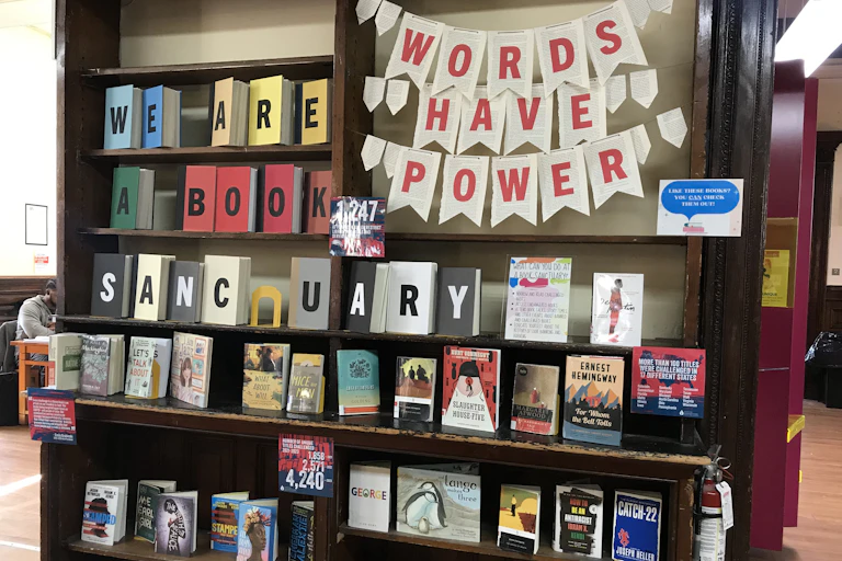 Shelves of books with a banner reading 'Words Have Power' andn a sign pronouncing the library 'a sanctuary for banned books.'