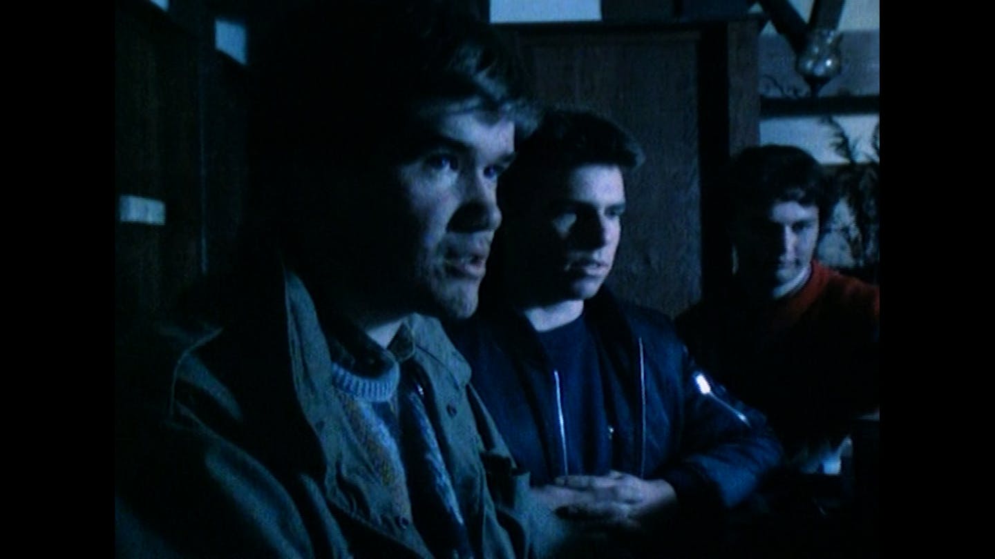 Three young boys in a dark room speak to someone off-screen.