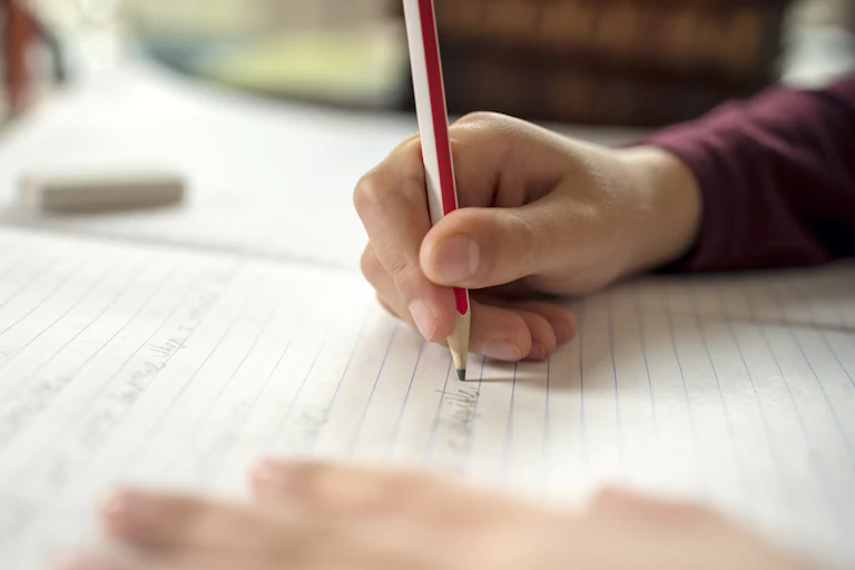 A child writes on a notepad with a pencil.