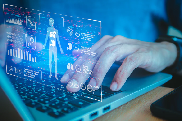 A person types of a laptop keyboard. Superimposed over their hands is a graphic of a human body and its health information.