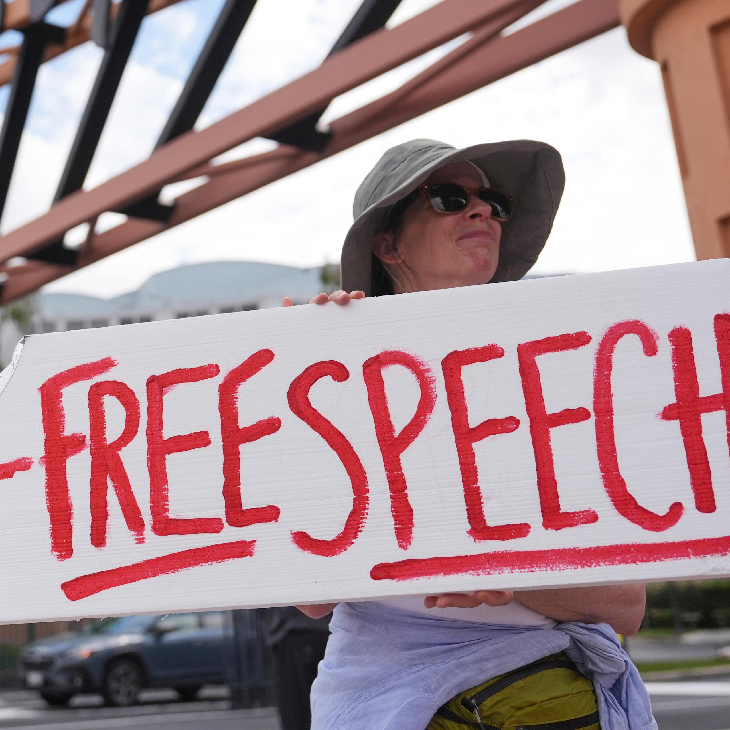 A demonstrator holds a sign that reads Free Speech.