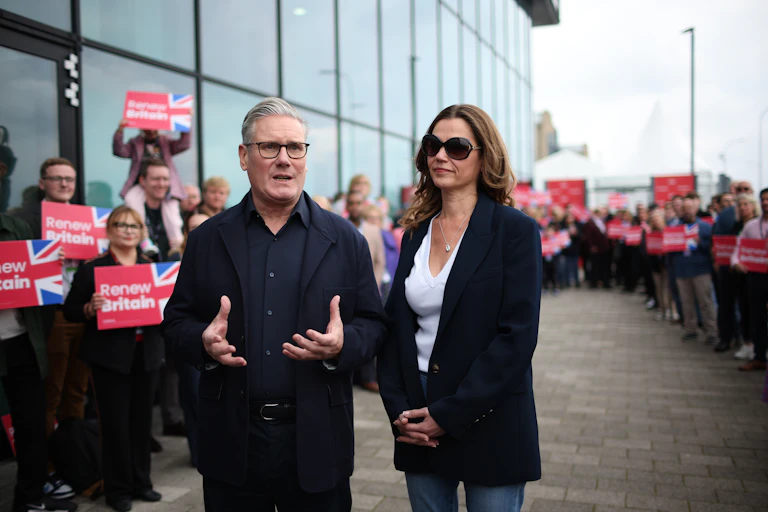 Keir and Victoria Starmer walking in front of supporters holding signs that read 'renew Britain'.