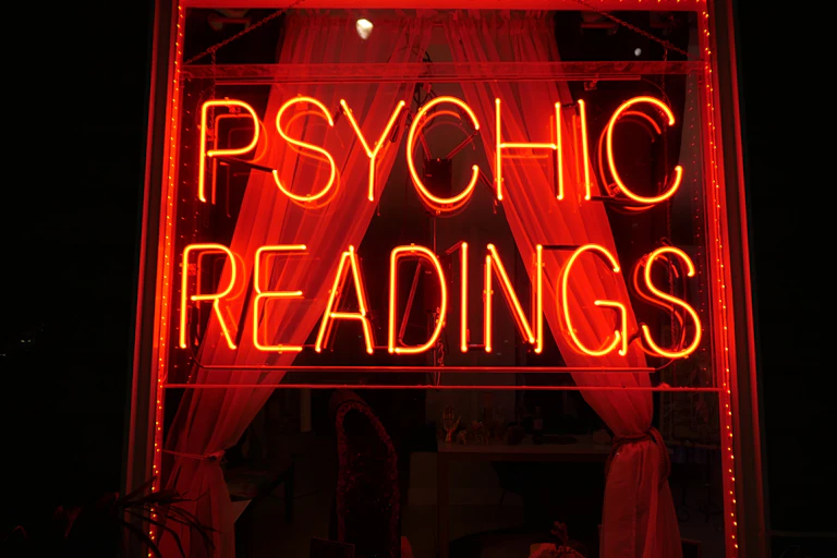 A red neon sign reading 'Psychic Readings' in a dark window