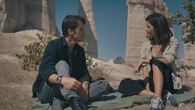 Una pareja habla delante de unas ruinas.