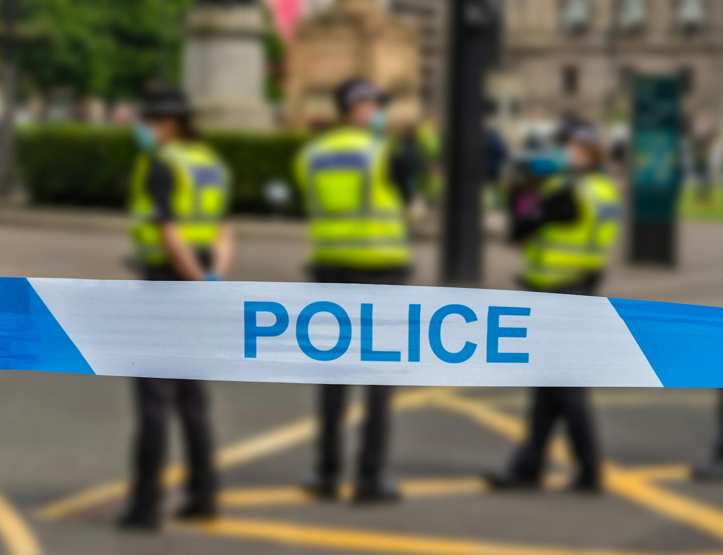 police tape with three uniformed officers in the background