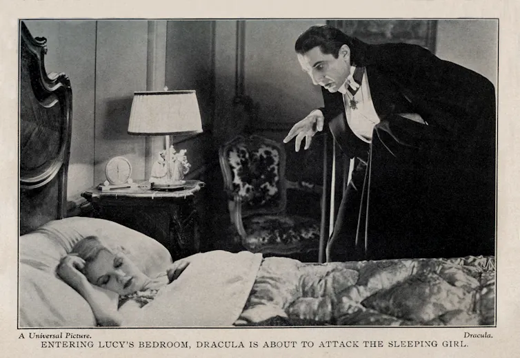 A black-and-white photo shows a woman lying in a bed sleeping, while a man wearing a black jacket and white shirt leers over her.