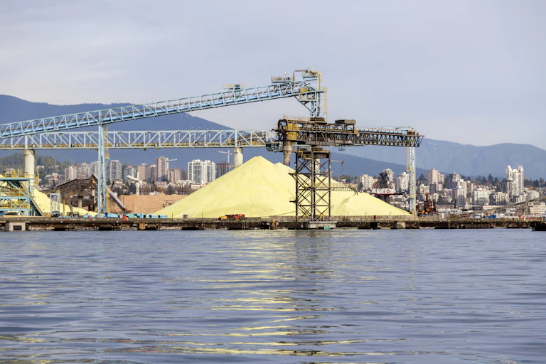 A pile of sulfur sits near a crane at a seaport.