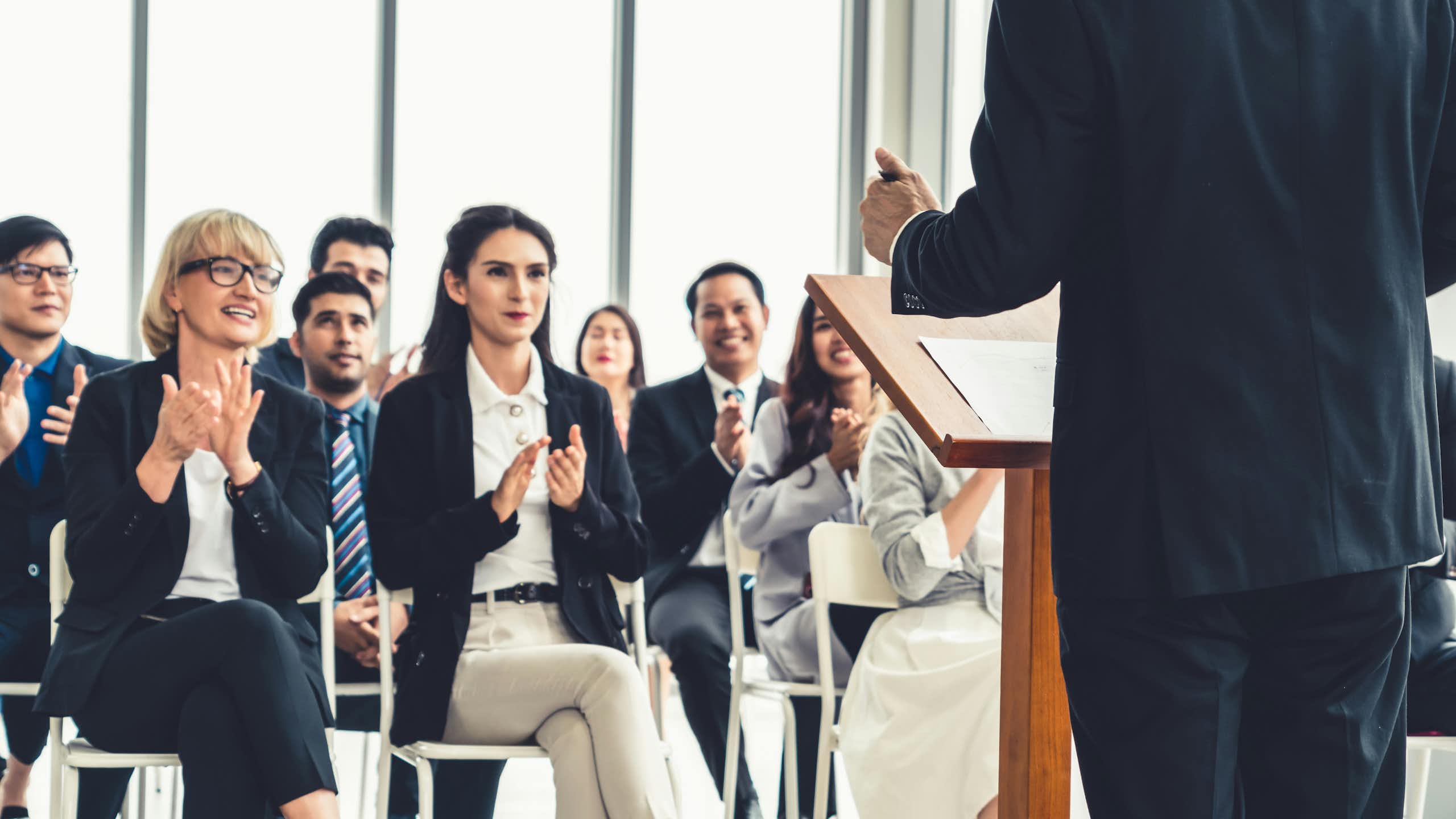 A person, seen from behind, speaks to an audience of people