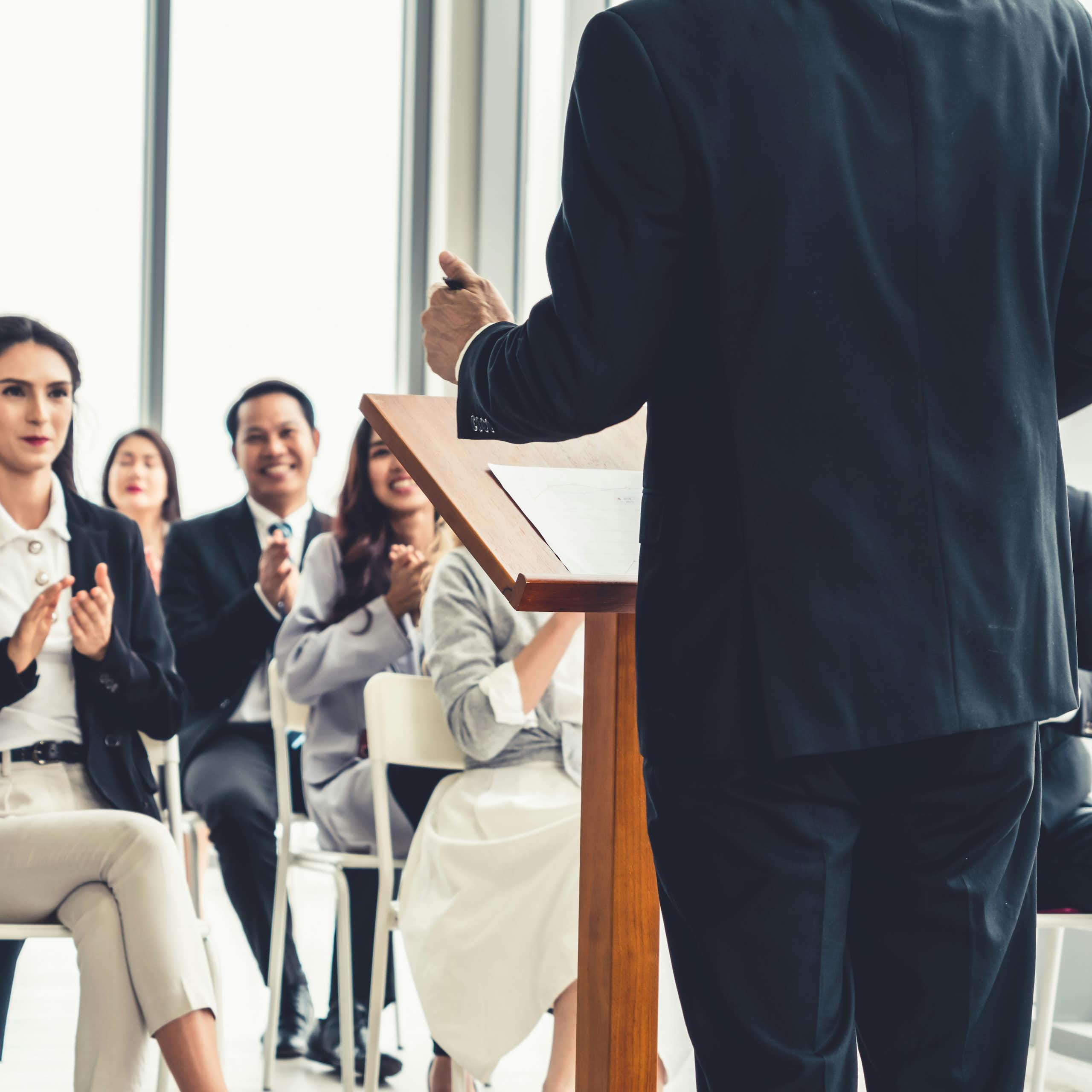 A person, seen from behind, speaks to an audience of people