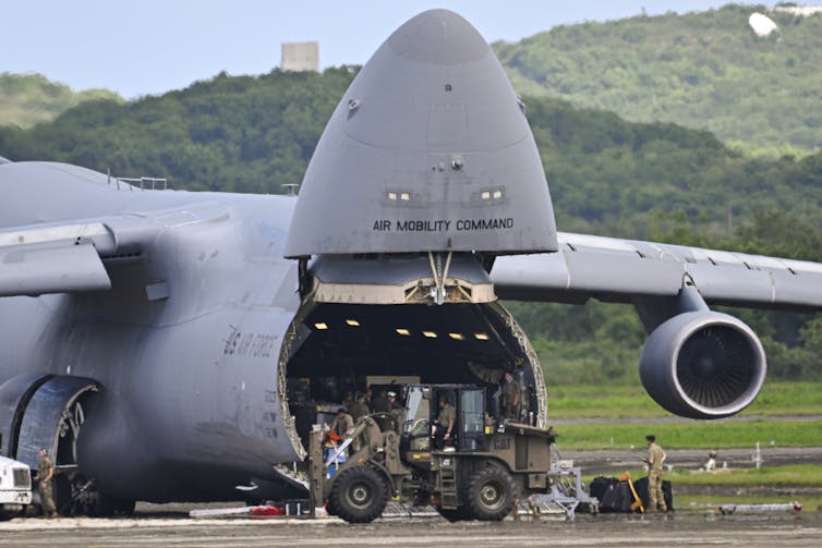 A large cargo plane being unloaded by soldiers.