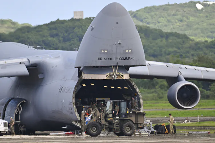 A large cargo plane being unloaded by soldiers.