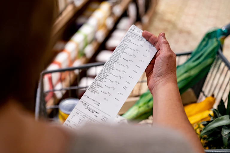 A woman with a shopping trolley looking at a receipt