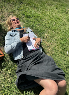 A woman lies on the ground, holding a drawing pad to her tummy.