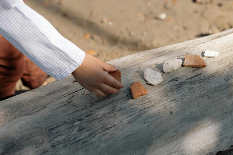 A young child places small stones on a log.