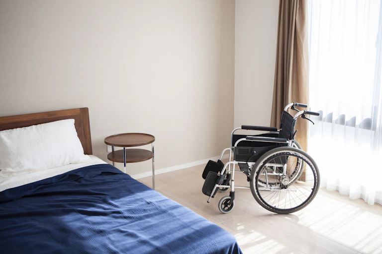 Sun streams onto empty bed and a wheelchair.