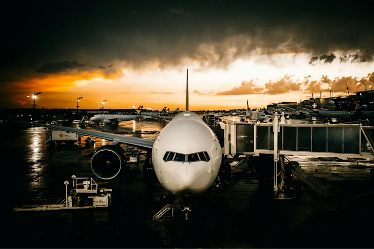 A parked airliner under dramatic stormy skies at sunset.