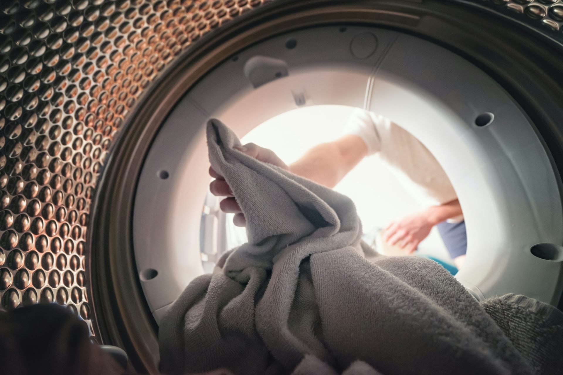 une personne est en train de remplir son lave-linge; la photo est vue depuis l'intérieur du tambour.