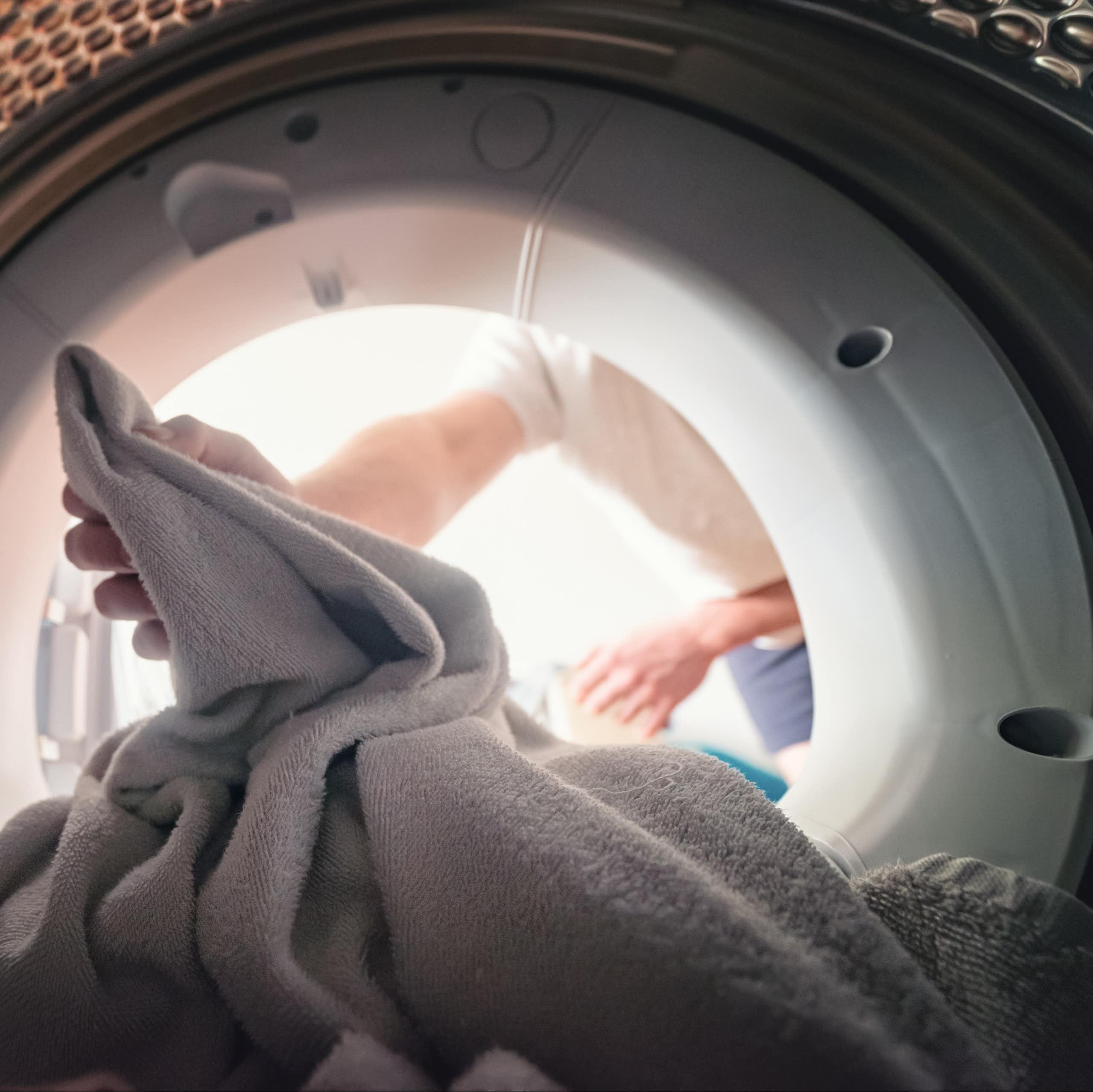 une personne est en train de remplir son lave-linge; la photo est vue depuis l'intérieur du tambour.