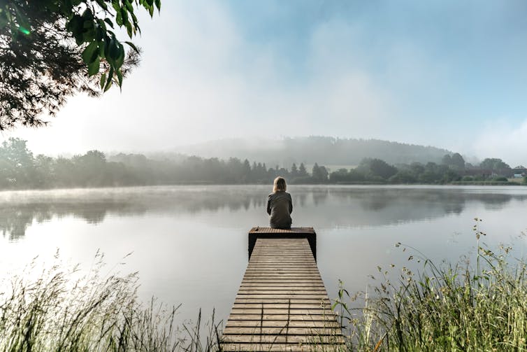 One person sitting alone at the end of a jetty on the side of a misty lake