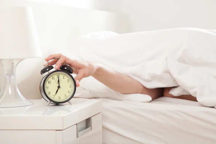 Hand reaching out from bedcovers to turn off alarm clock.