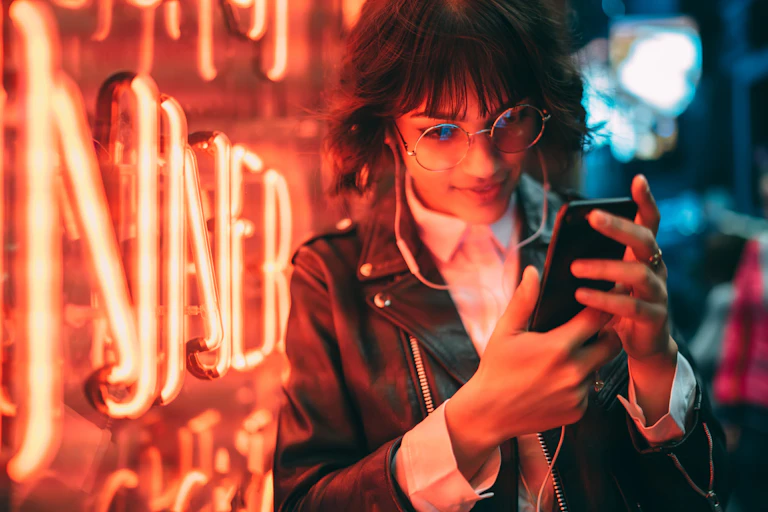 young woman listening to music on her phone in front of some neon lights