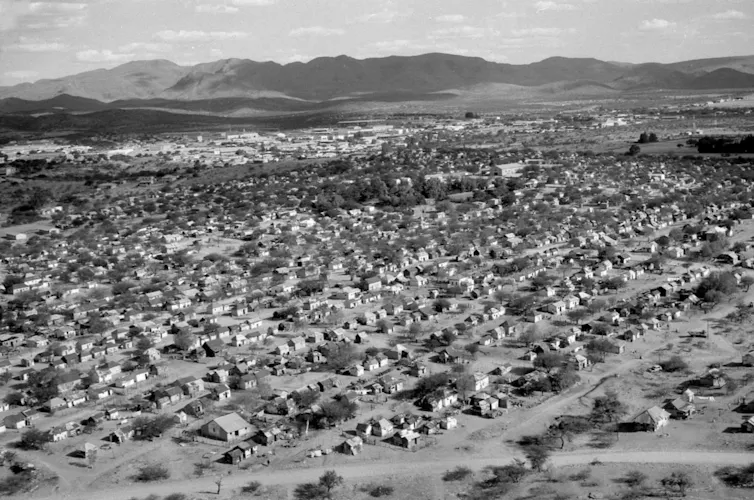 A black and white photo of rows and rows of small houses against the backdrop of a mountain.
