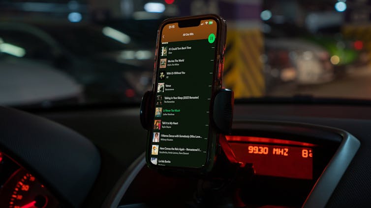 mobile phone screen mounted on a car dashboard and showing a spotify playlist