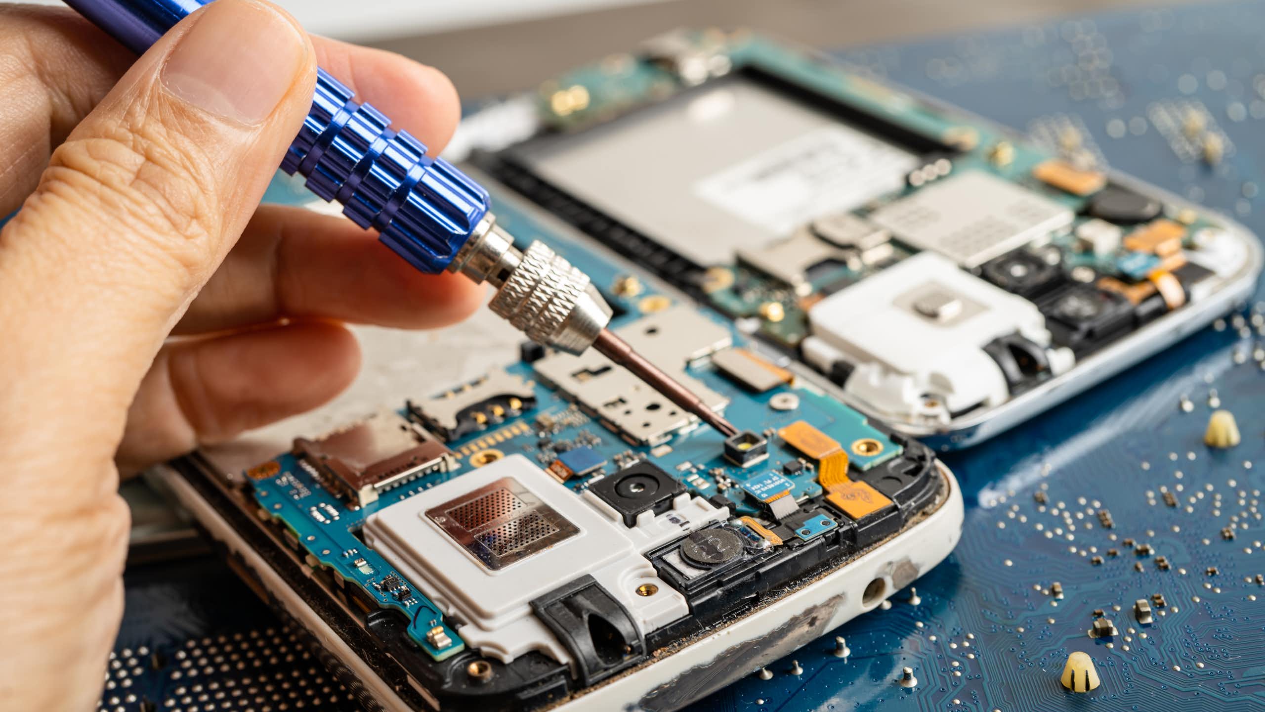 A person's hand holding a precision tool is visible above the inside of a smartphone.